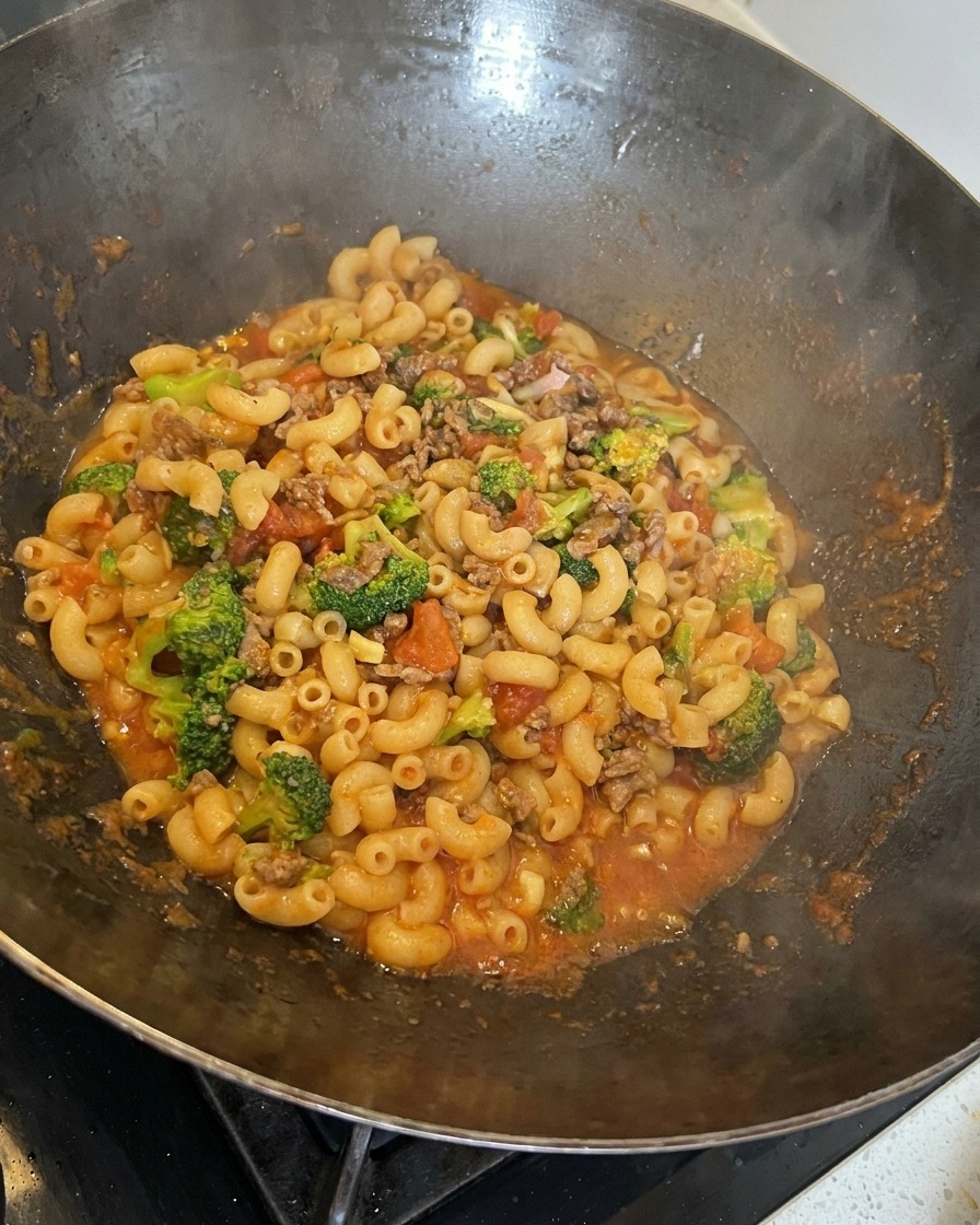 Pasta, beef, broccoli, and melting cheese being stirred together in a large wok.