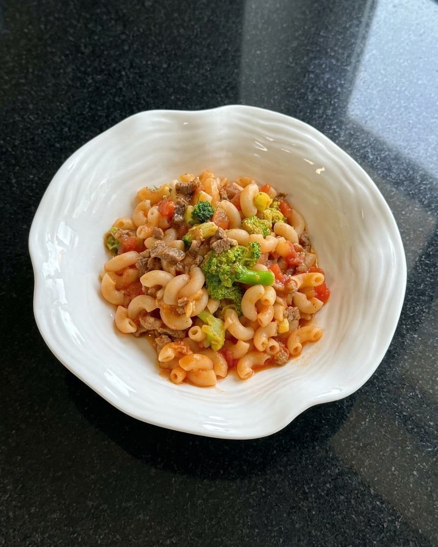 Finished macaroni dish plated in a white bowl, being garnished with dried herbs.