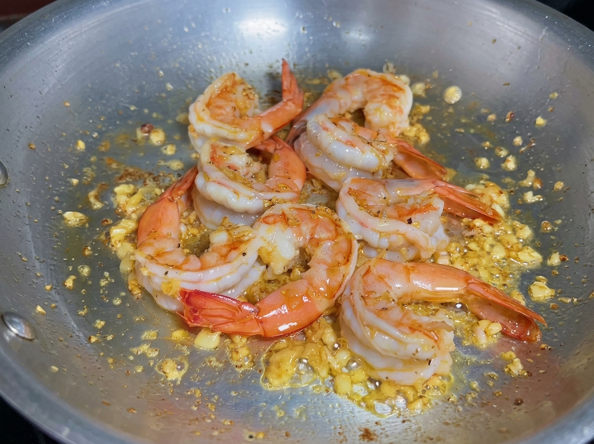 Liquid being poured into a pan with cooked shrimp to deglaze and collect flavors.