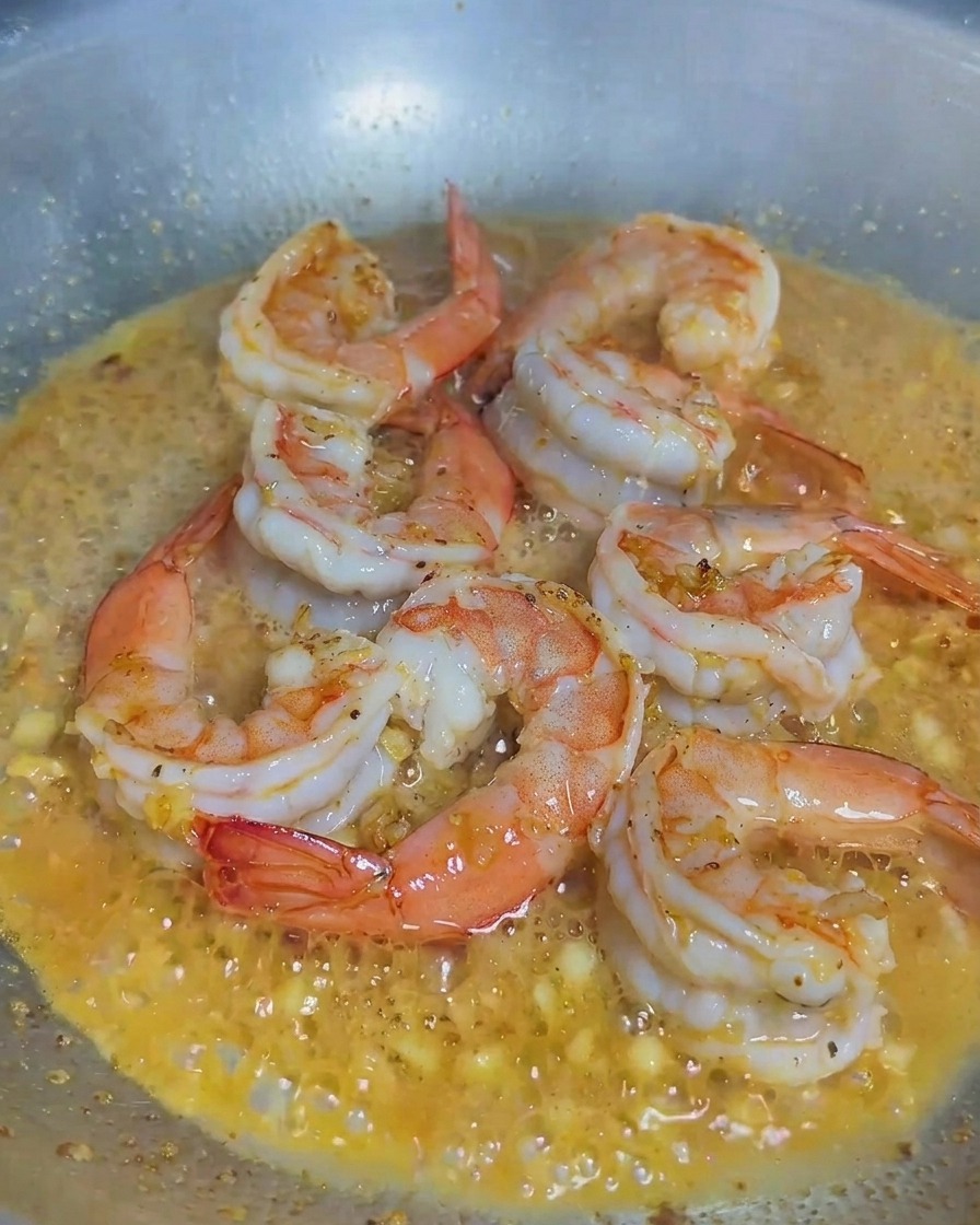 Cream being poured into a pan containing cooked shrimp and minced garlic.