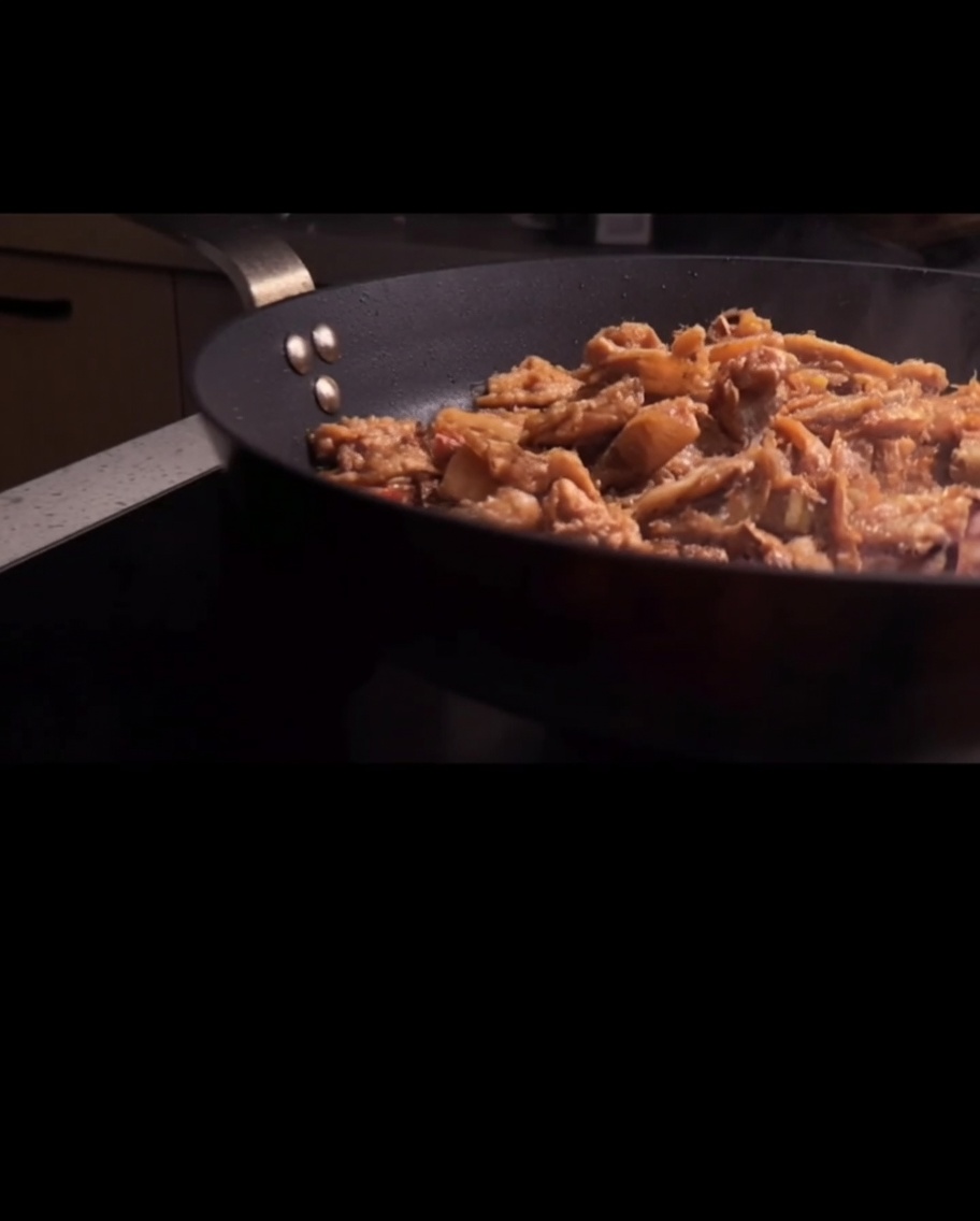 Spaghetti being tossed with the meat sauce in a pan.