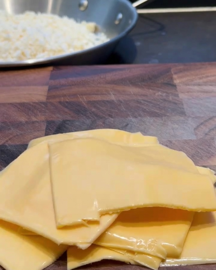 Slices of cheddar cheese being cut into smaller pieces on a wooden board.
