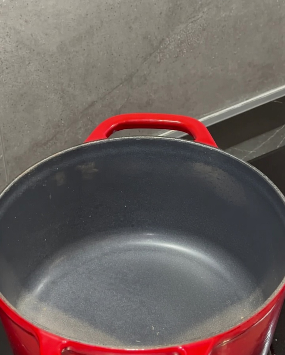 A block of butter melting in a red pot on the stove.