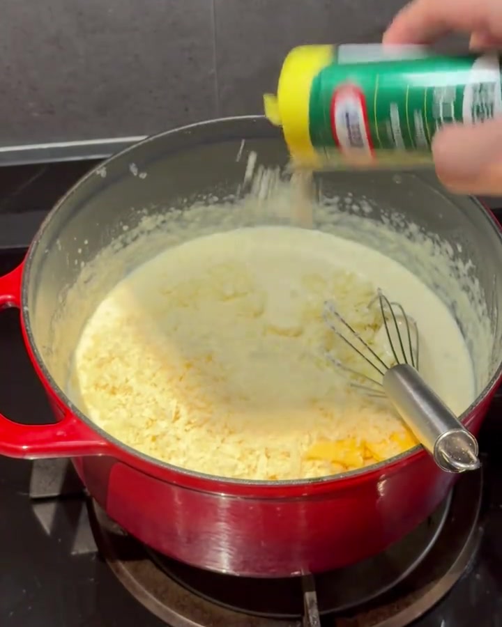 Cheese powder being whisked into a creamy sauce in a red pot.