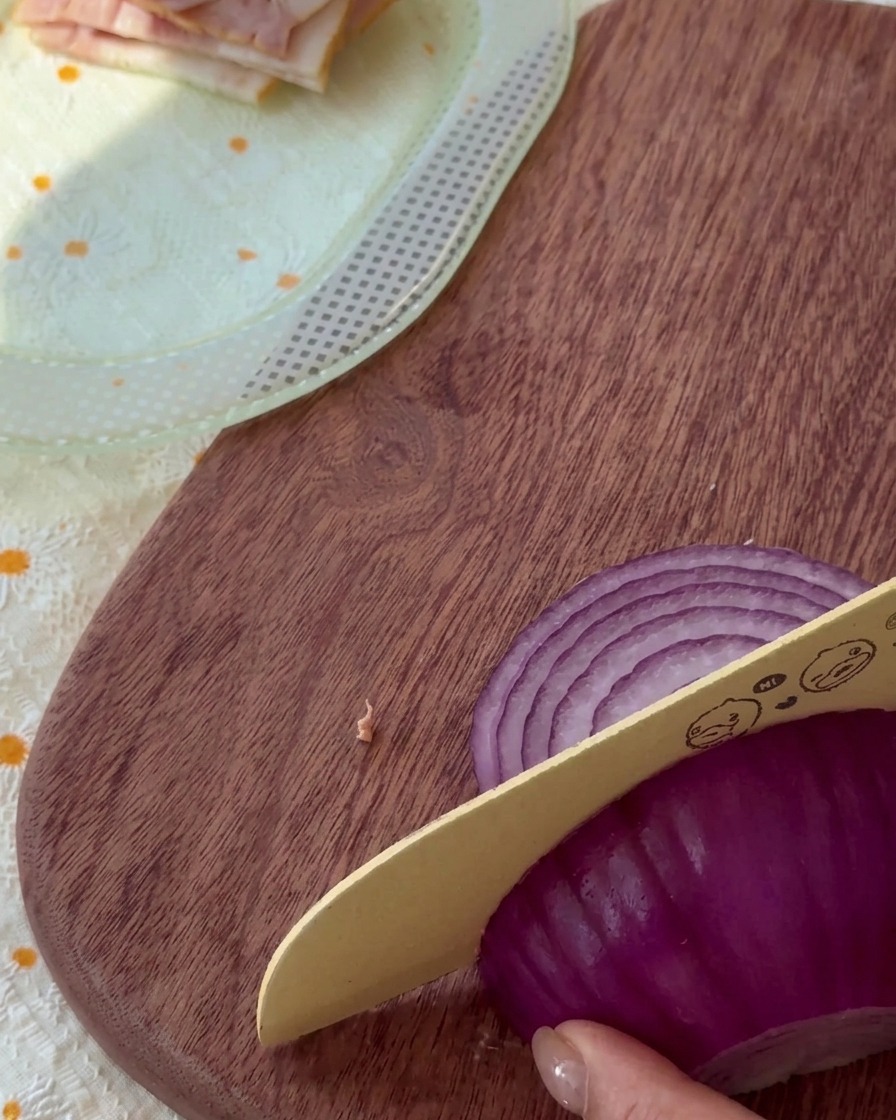 Thinly shredded raw red onion pieces on a wooden cutting board.