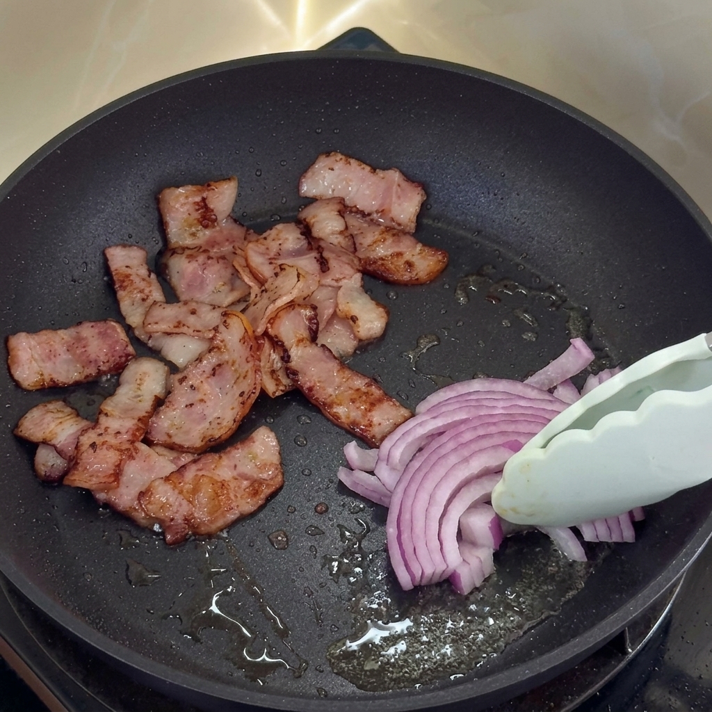 Sliced red onions cooking in bacon fat next to crispy bacon.