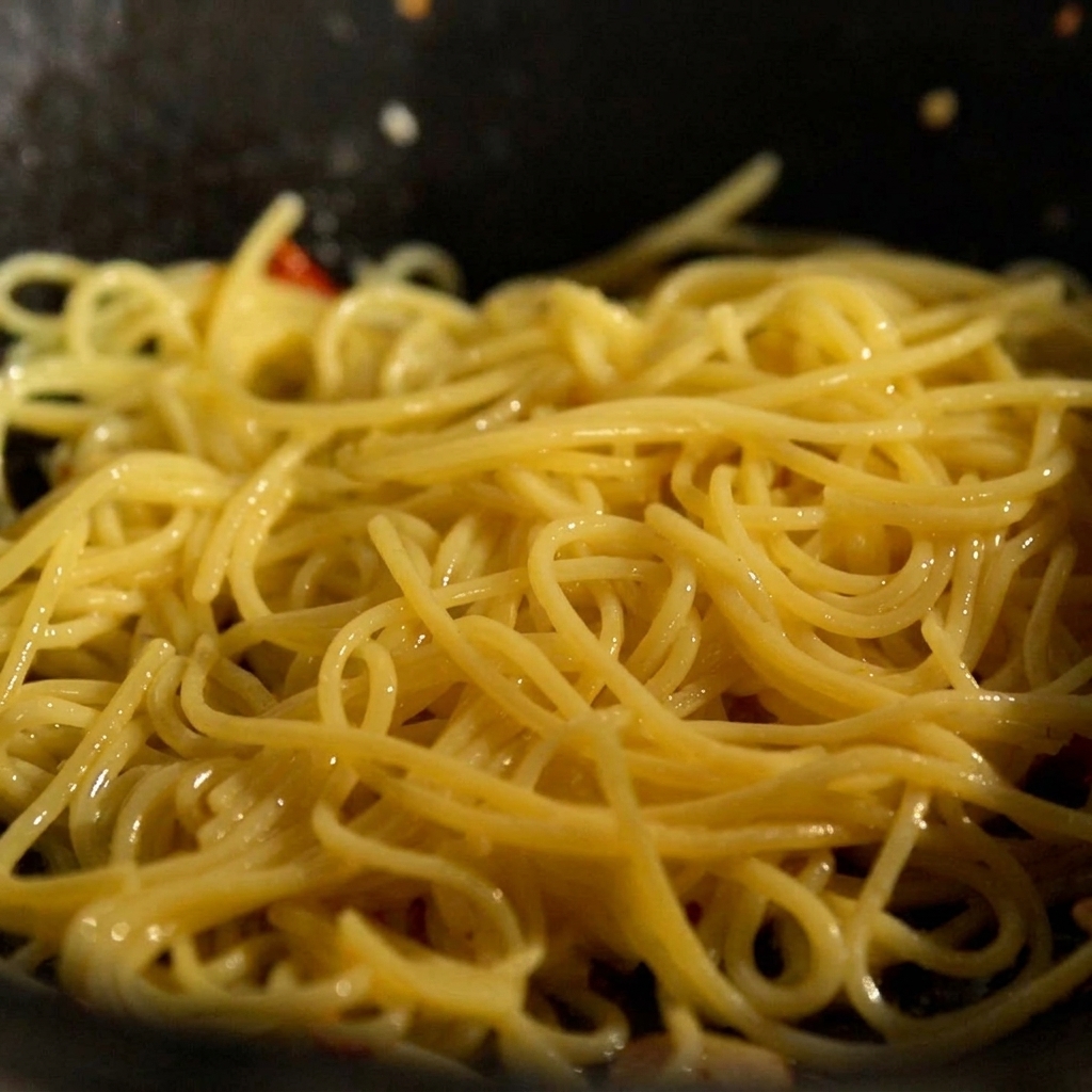 Cooked noodles and a knob of butter being added to a pan with sautéed garlic and chili.