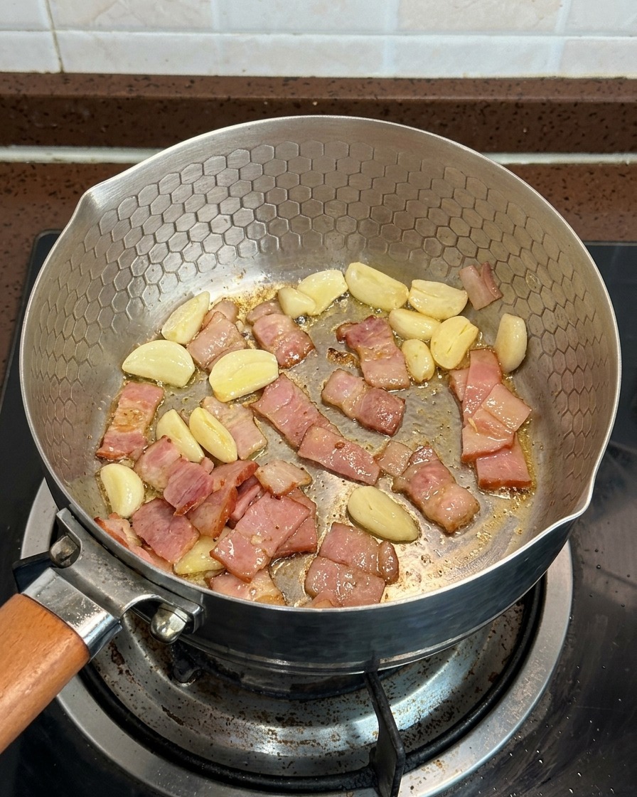 Sliced mushrooms, bacon pieces, and garlic slices cooking together in a pan.