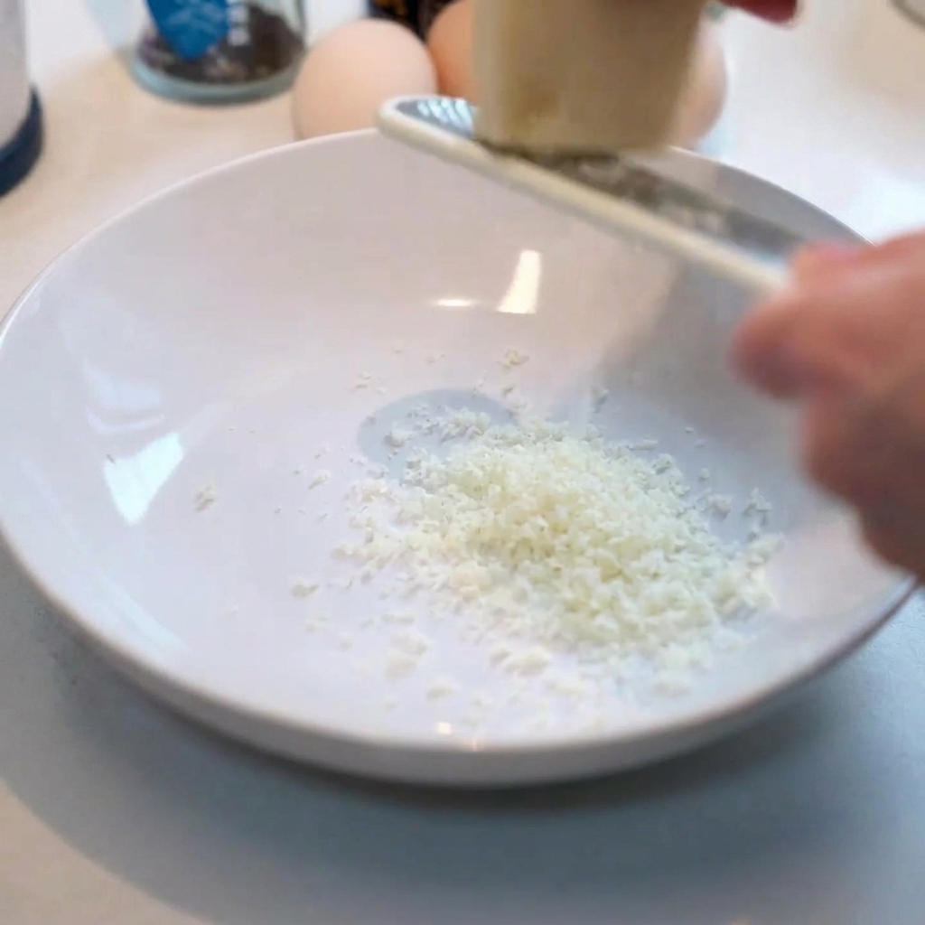 Grating fresh Parmesan cheese into a clean white bowl.