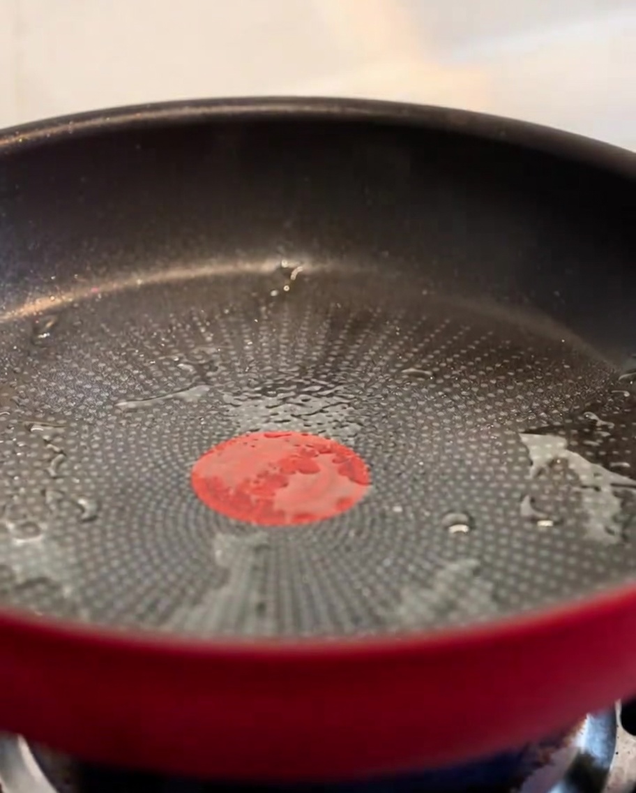 Crispy bacon bits sizzling in a red pan.