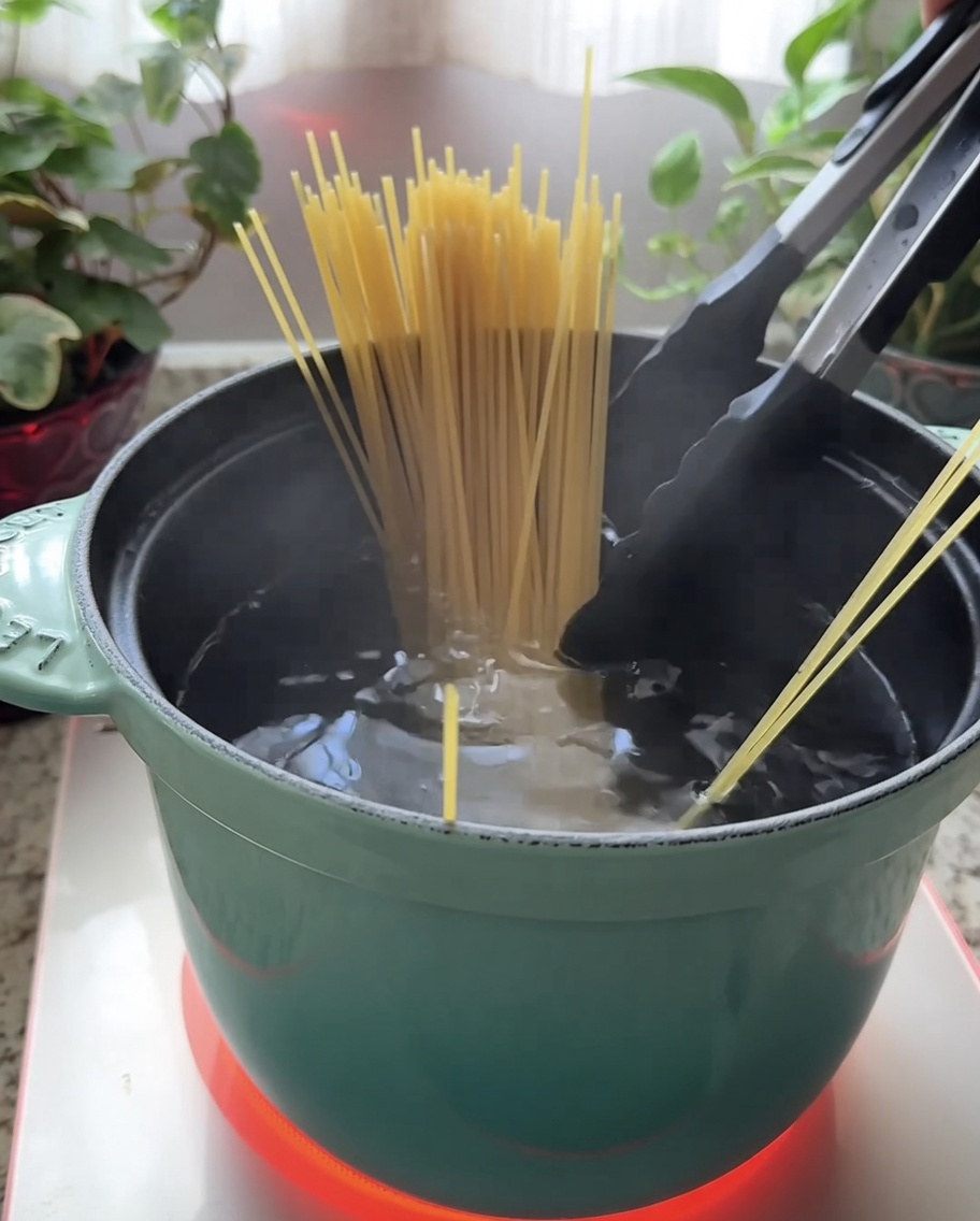 Dry spaghetti being submerged into a teal pot filled with boiling water.