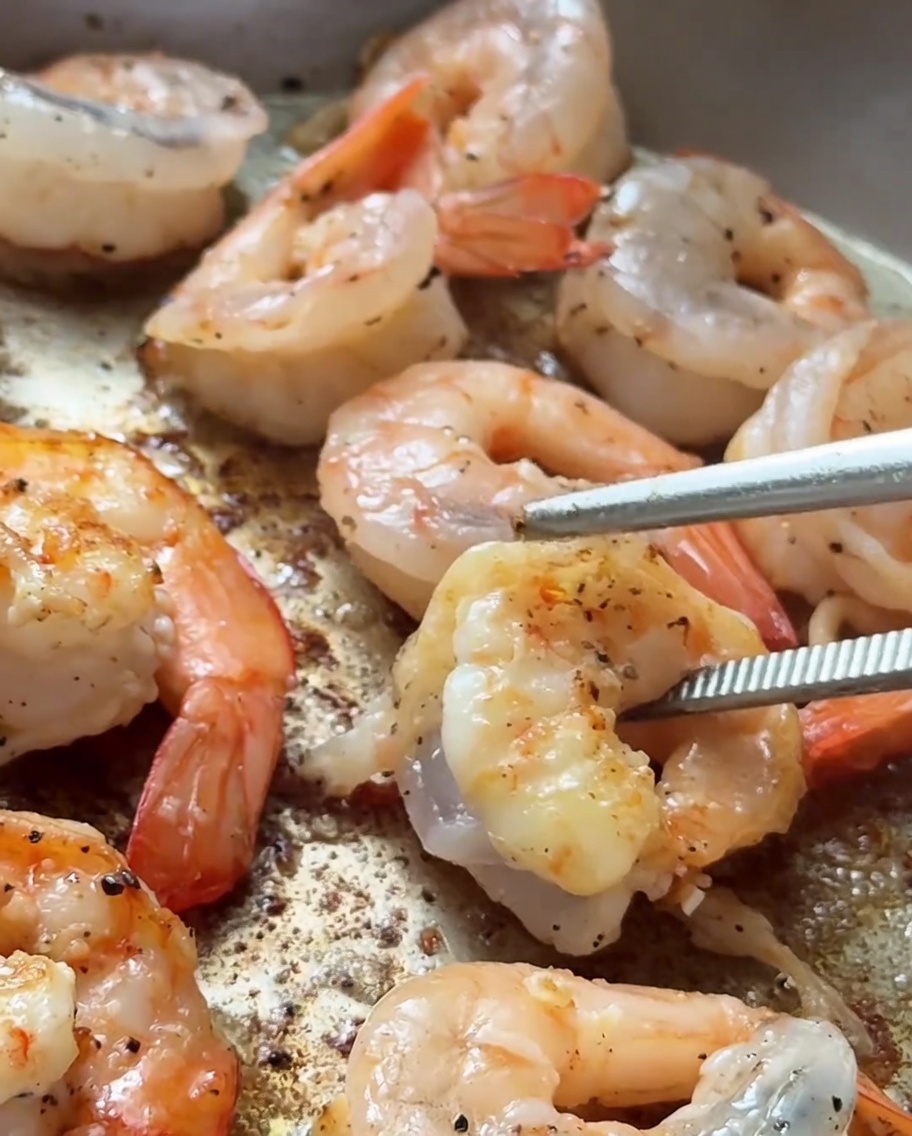 Shrimp searing in a hot pan with visible golden-brown coloring on the edges.