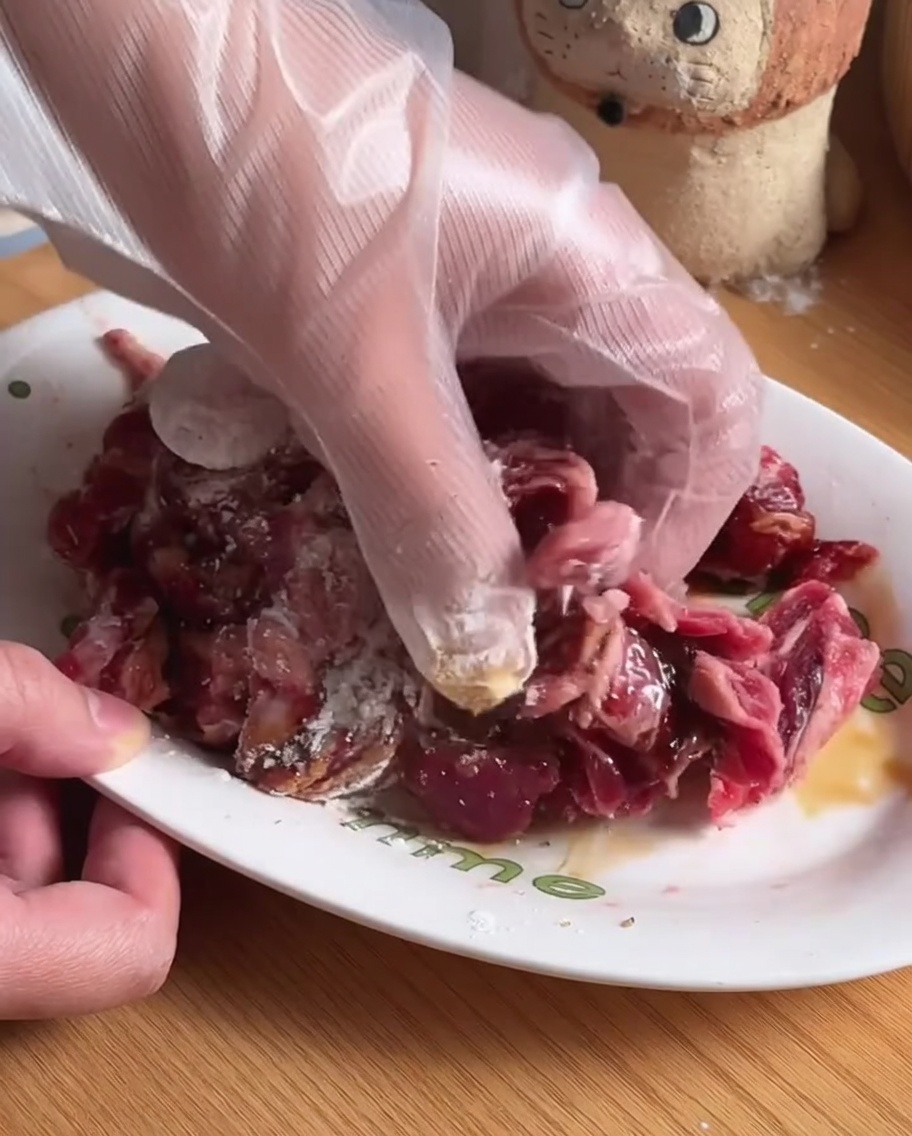 Beef strips being mixed with seasonings and marinade ingredients in a white bowl.
