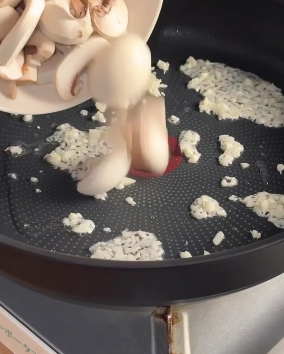 Sliced mushrooms being added to the pan with sautéed garlic.