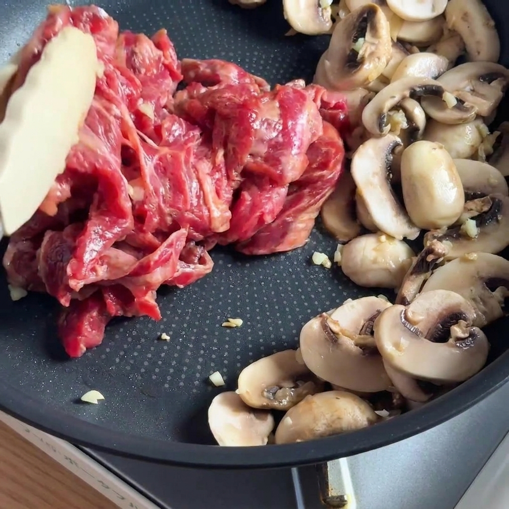 Marinated beef strips stir-frying in a pan with sliced mushrooms.