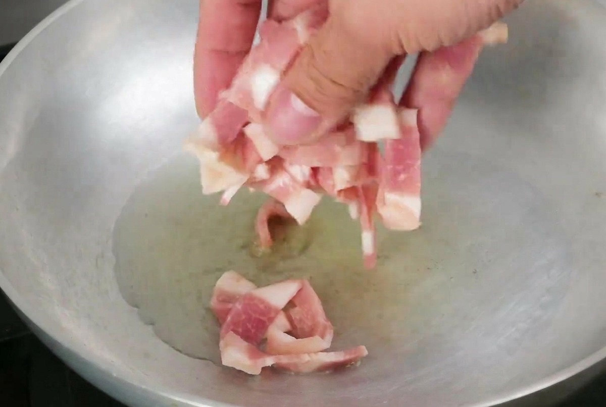 Bacon strips frying in a pan with shimmering olive oil.