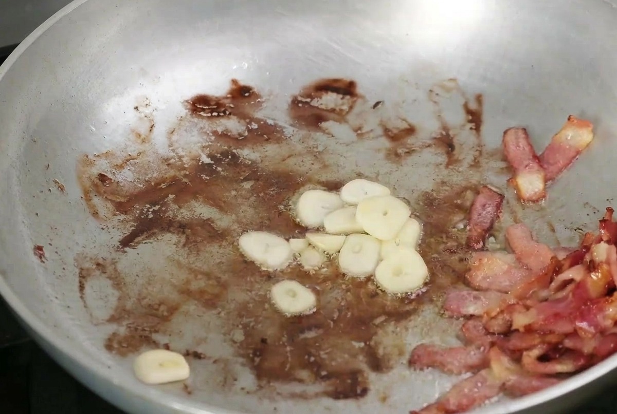 Sliced garlic and mushrooms browning in a pan alongside crispy bacon.