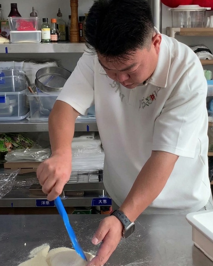 A portion of raw pizza dough being lifted from a white container with a blue scraper.