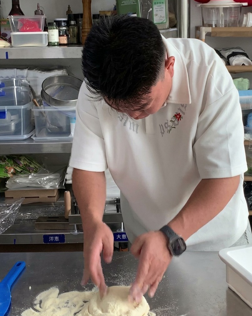 Hands pressing down on a ball of raw dough to begin forming a flat, round pizza base.