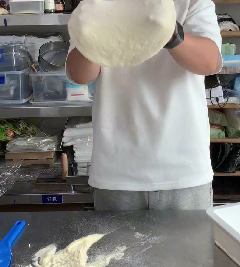 Pizza dough being stretched over the knuckles to increase its diameter and thin the center.