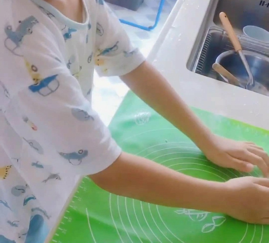 A ball of pizza dough being kneaded on a green silicone mat.