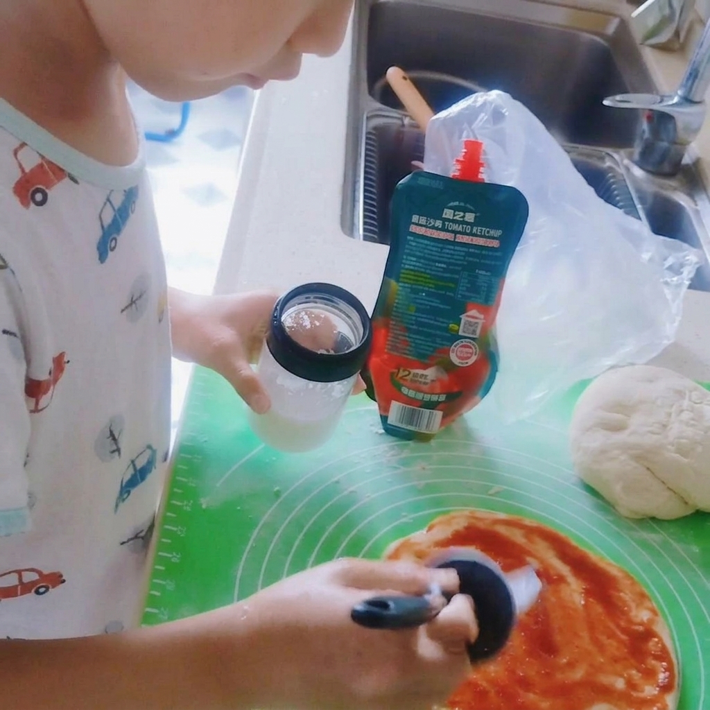 Salt being sprinkled over the tomato sauce on the pizza dough.