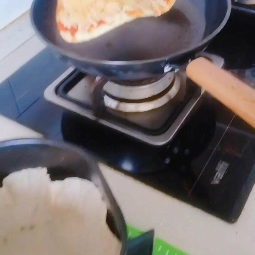 The pizza being carefully moved from the frying pan into an air fryer basket lined with parchment paper.