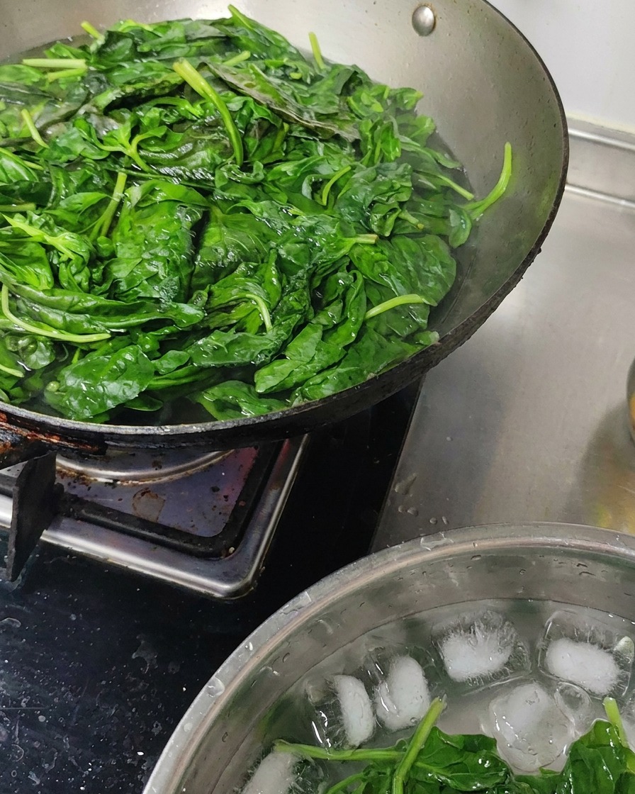 Blanched basil leaves being cooled in a bowl filled with ice water.