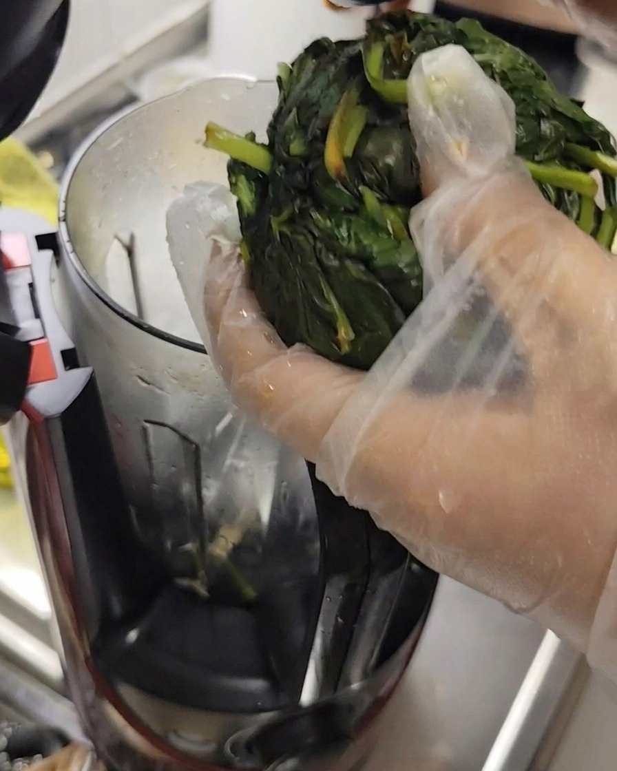 Basil leaves being squeezed of water while wearing gloves, preparing them for the food processor.