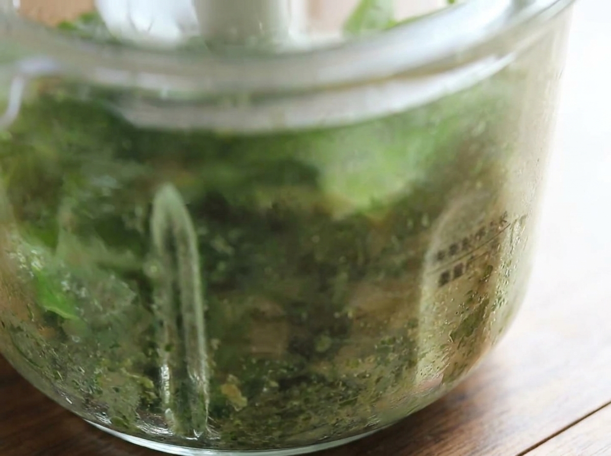 A close-up view of the food processor bowl showing the freshly blended, bright green basil pesto.