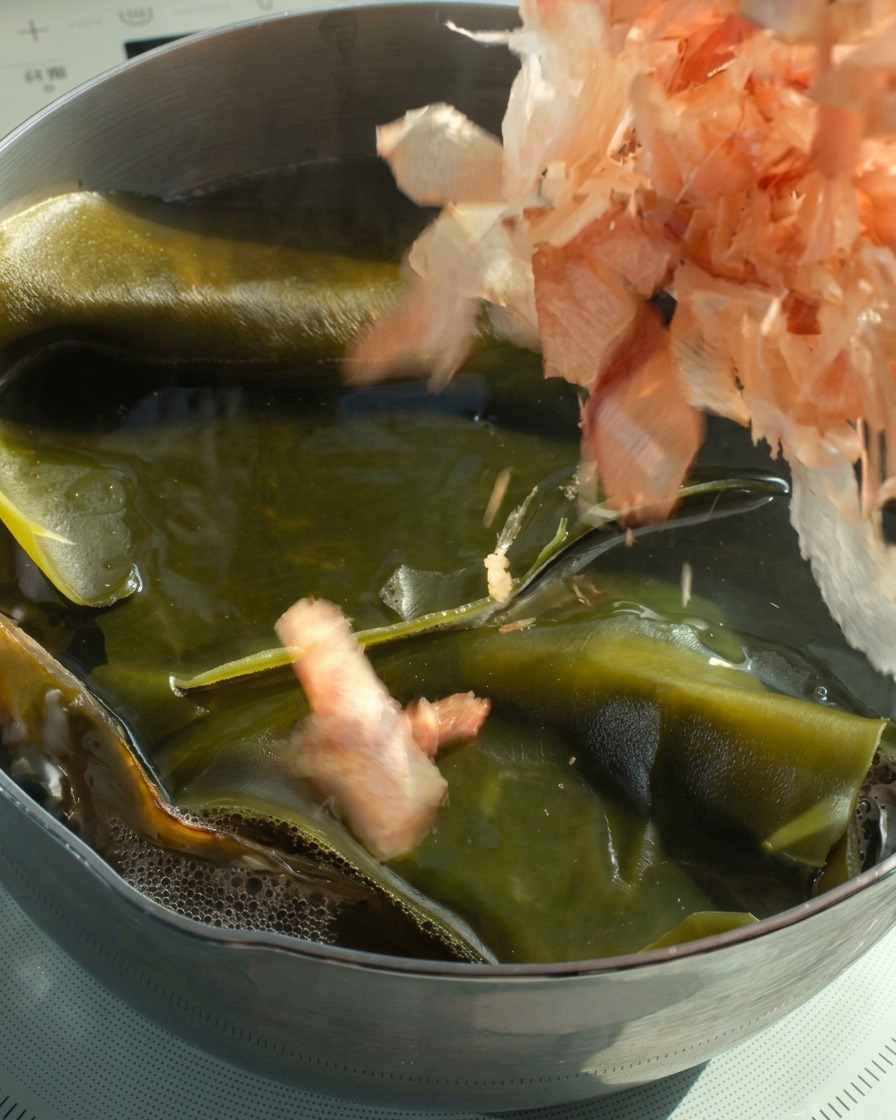 Bonito flakes being dropped into a pot of hot kombu stock.