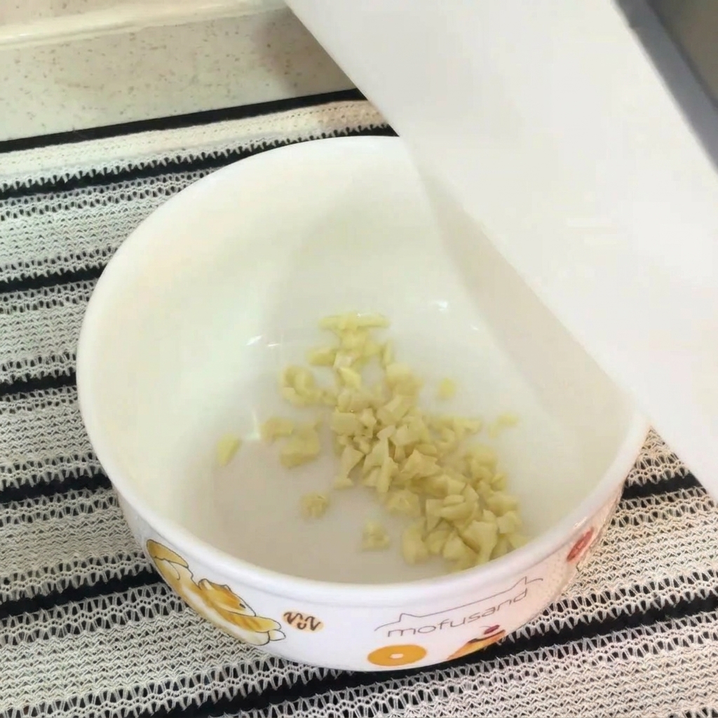 A close-up of a white bowl containing minced garlic, raw egg yolk, instant noodle seasoning, and mayonnaise, ready to be mixed into a soup base.