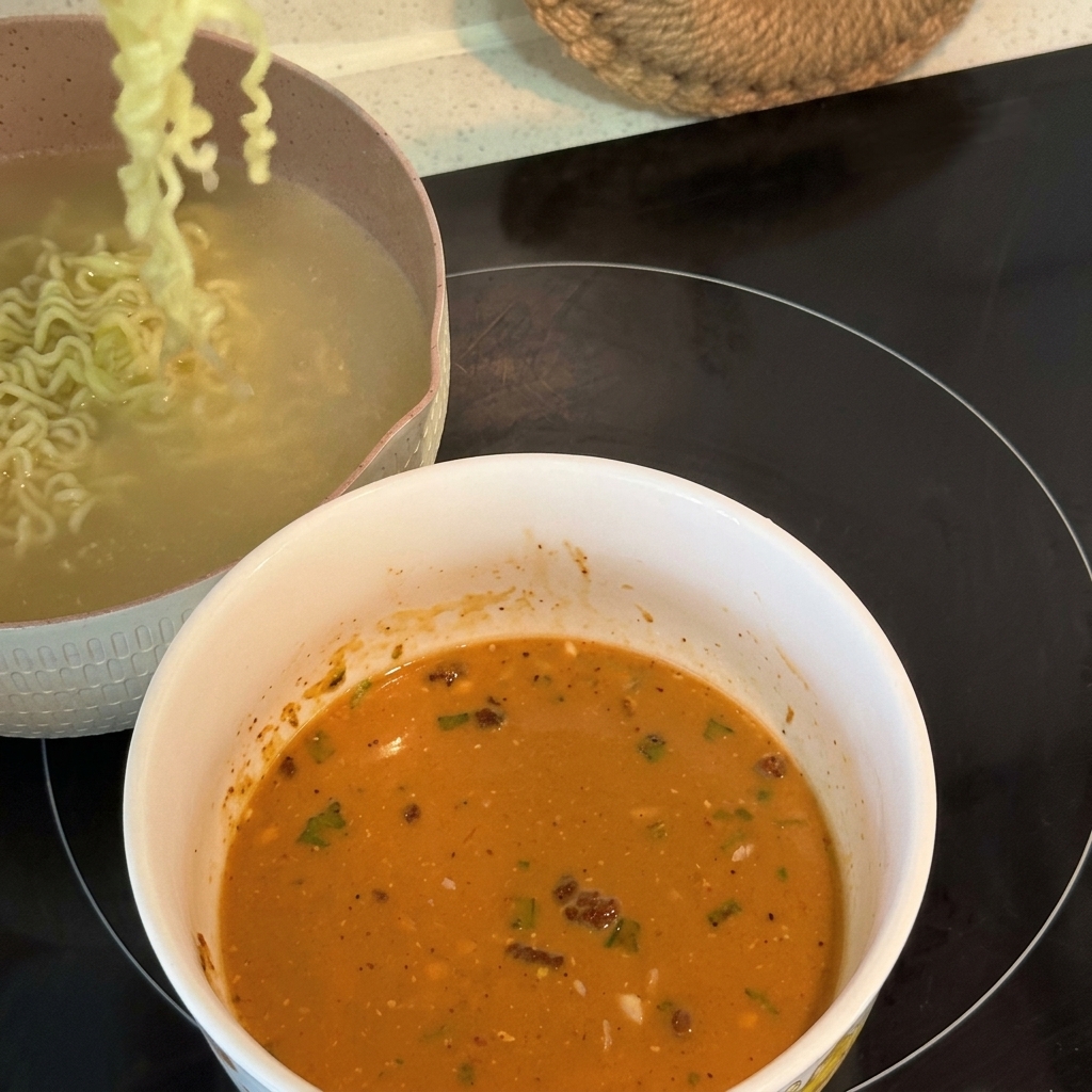 Cooked curly ramen noodles being lifted and transferred into a bowl filled with a creamy, emulsified soup base.