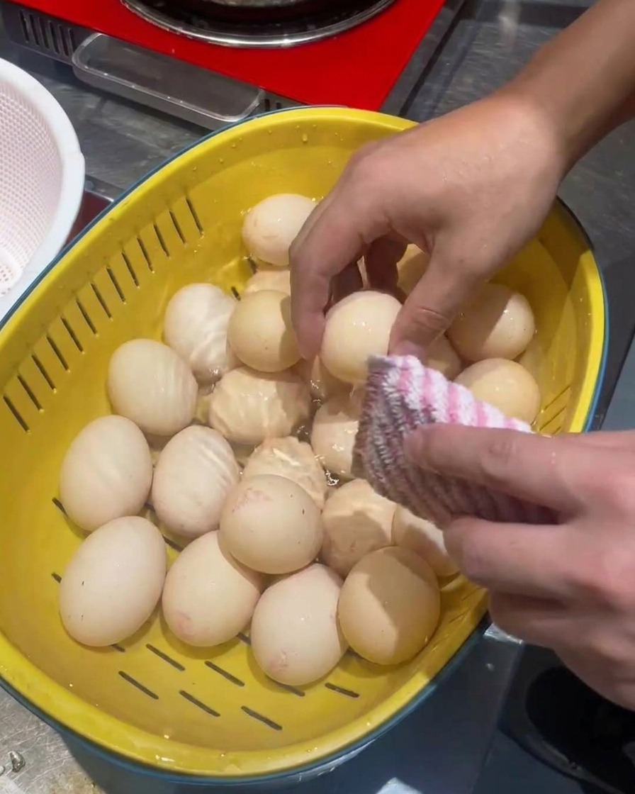 Eggs being cleaned in a yellow colander with a scrubbing pad.