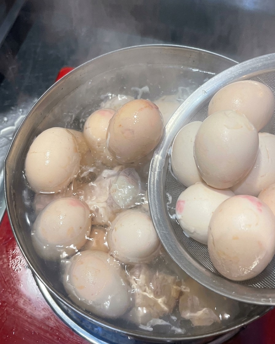 Boiled eggs being moved from a pot to an ice water bath.