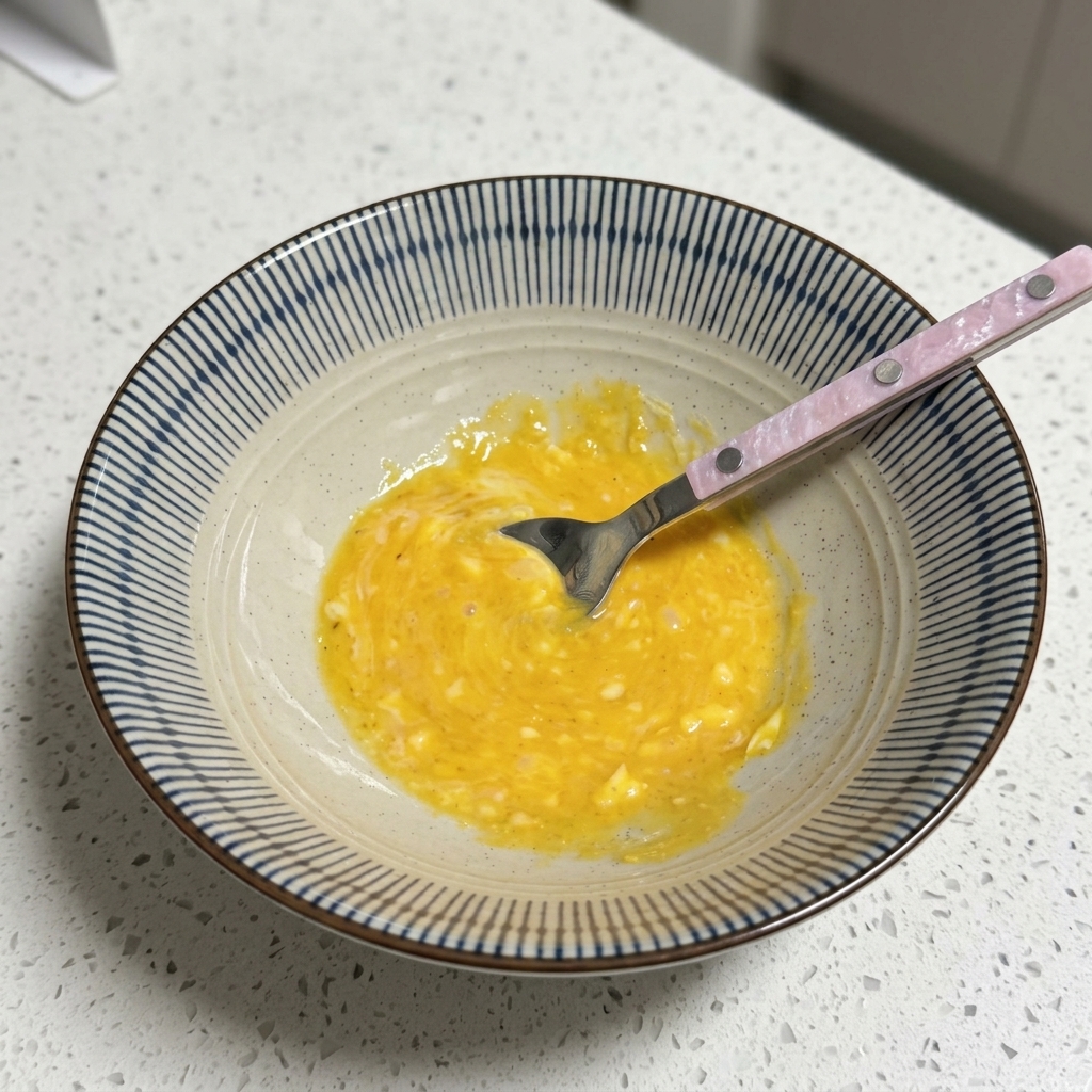 A bowl containing a yellow, creamy broth base being stirred with a spoon.