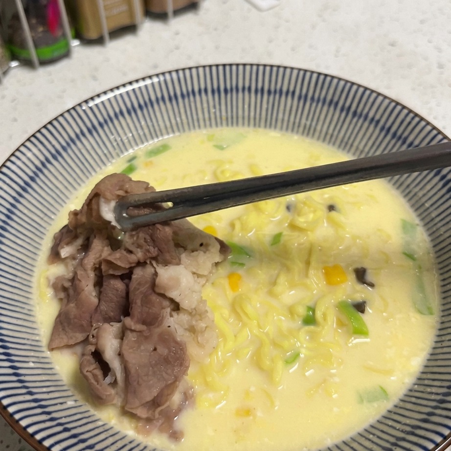 A spoonful of golden corn kernels being sprinkled over a bowl of ramen.