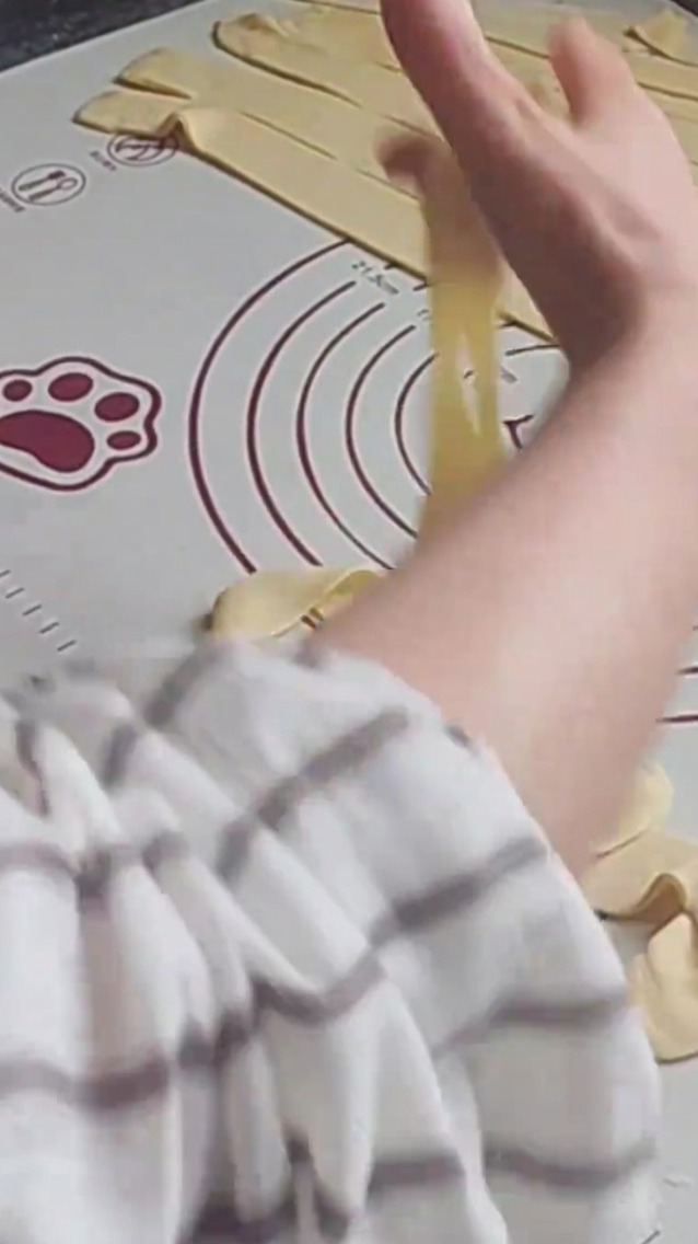 Hands stretching a strand of dough against a silicone mat, preparing it to be cooked.