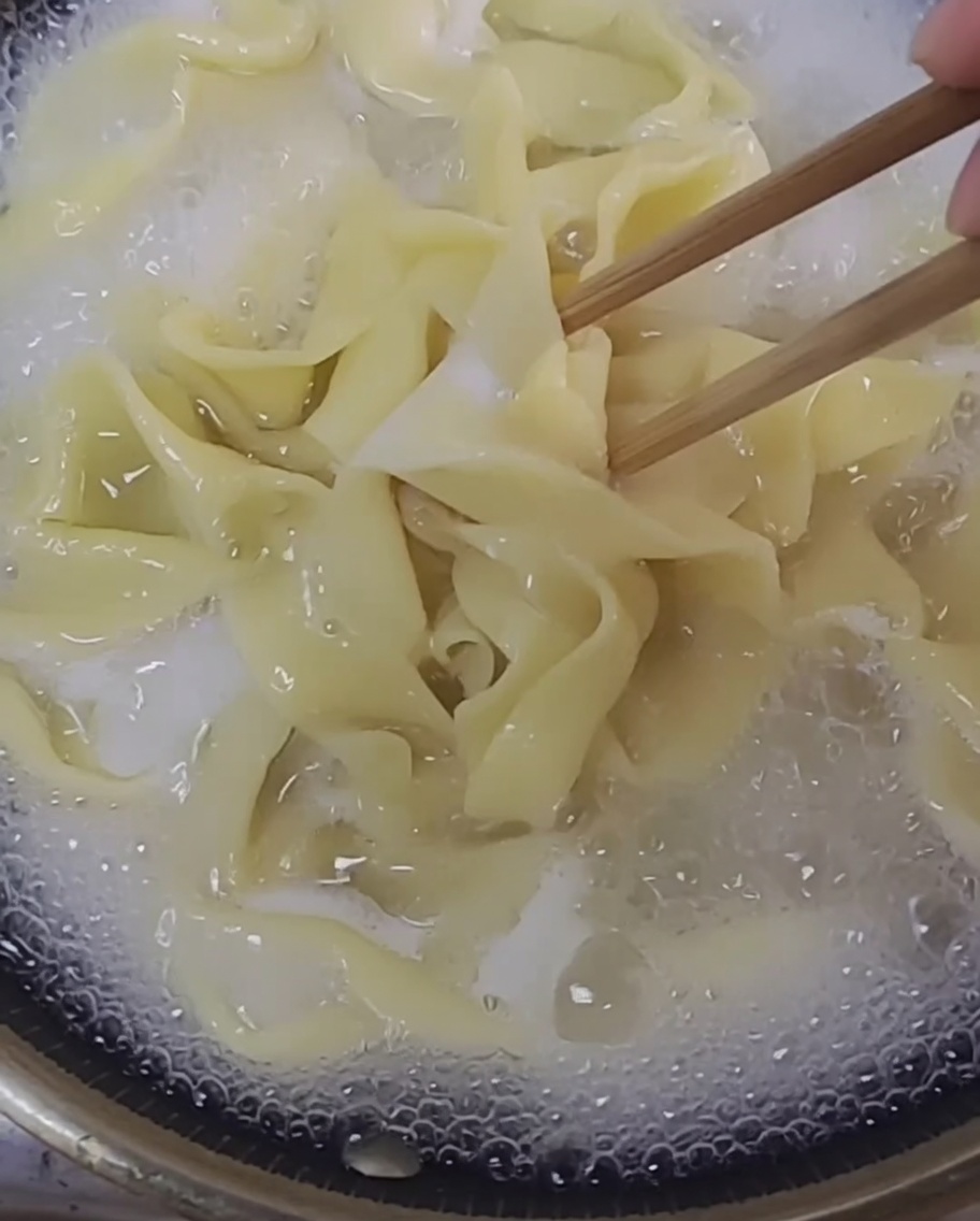 Freshly made noodle strands boiling in a clear pot of water.