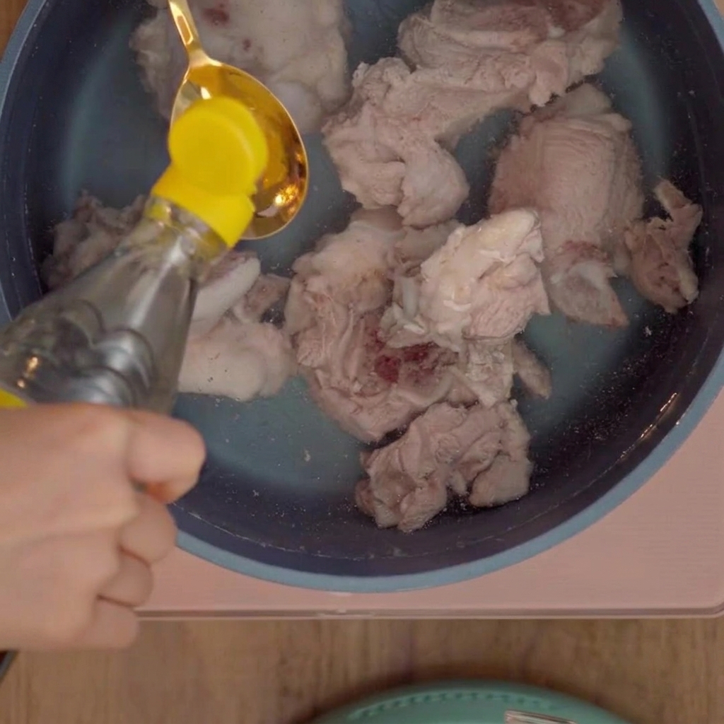 A tablespoon pouring white vinegar into a pot of pork bones.