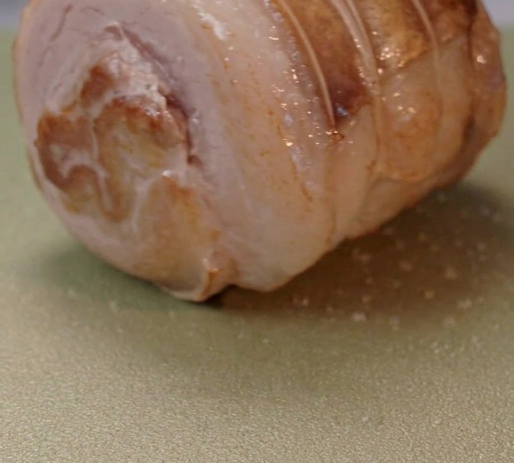 Rolled pork belly browning in a pan with hot oil.