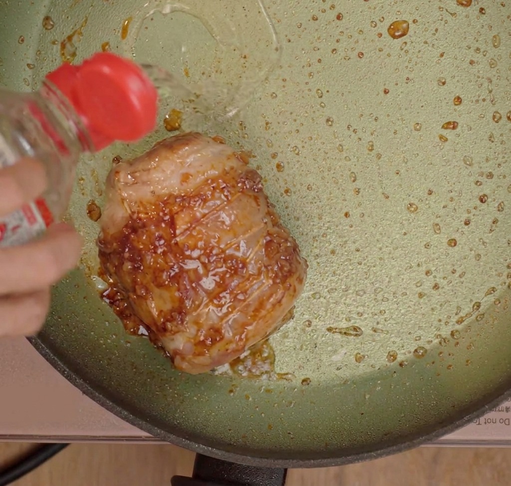 Liquid seasonings being poured over the seared pork belly in a pan.