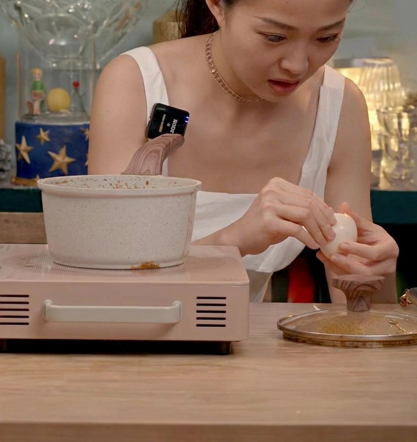 Peeled soft-boiled eggs being added to a pot filled with braising Chashu pork in a dark soy-based sauce.
