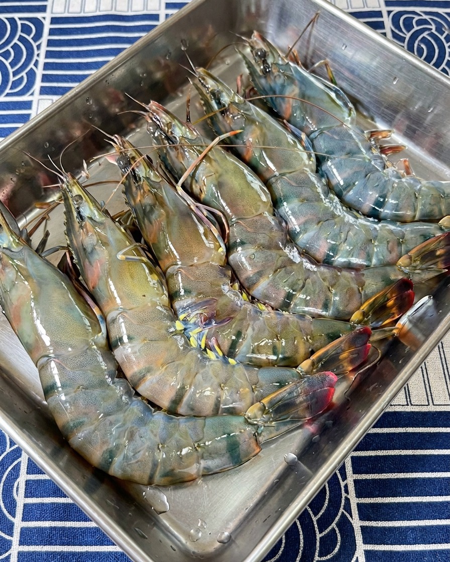 A collection of raw black tiger shrimp heads and shells resting in a stainless steel preparation tray.