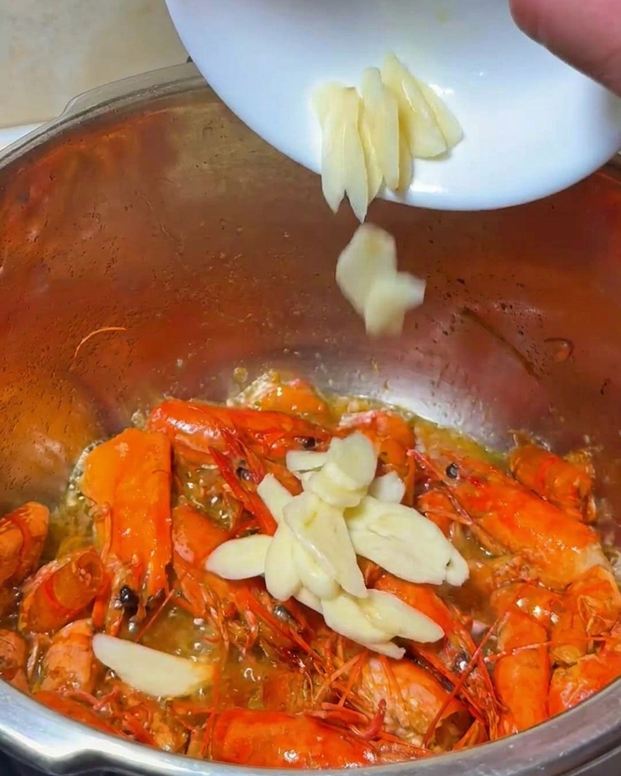 Sliced garlic and onion being added to the pot of frying shrimp shells.
