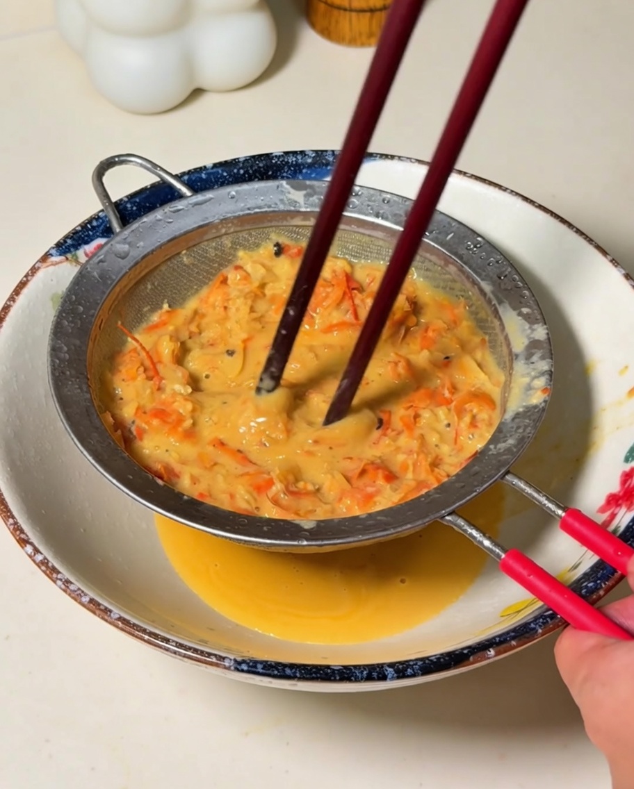 The blended orange mixture being strained through a fine mesh sieve into a bowl, pressed by chopsticks.