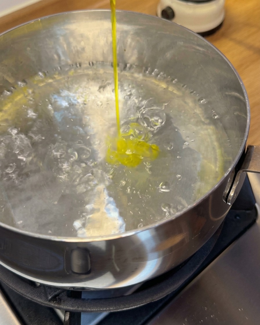 Raw shrimp wontons being lowered into a pot of boiling water using a slotted spoon.