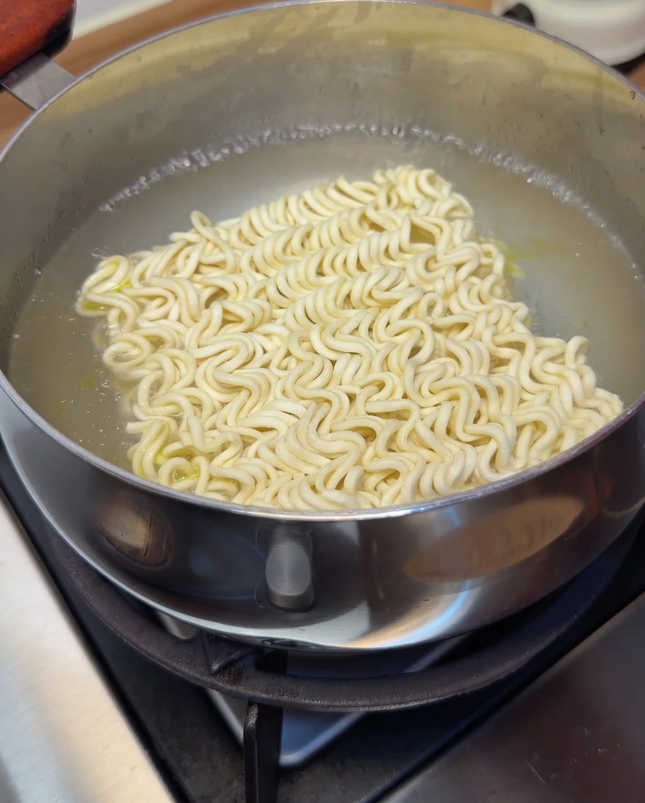 A block of instant noodles submerged in boiling water, cooking until tender.