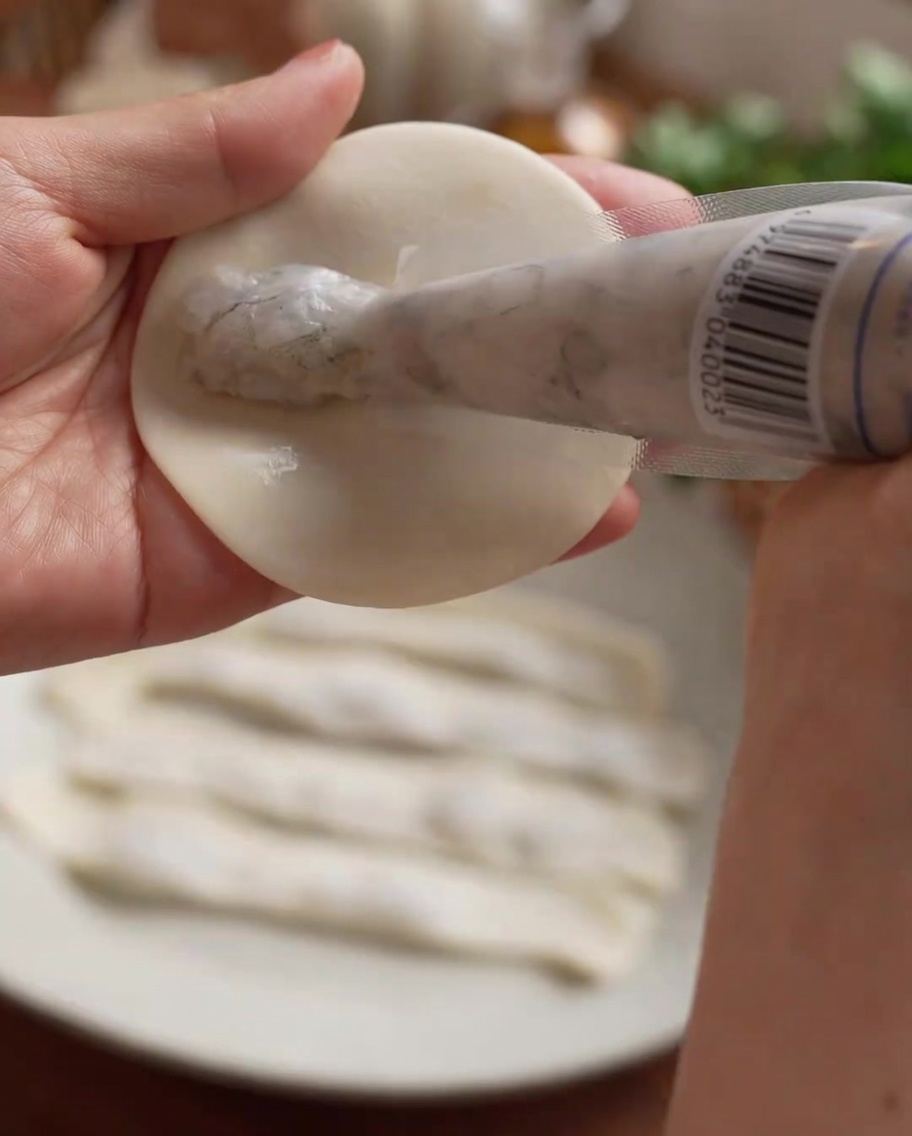 Shrimp paste being piped into a straight line onto the center of a dumpling wrapper.