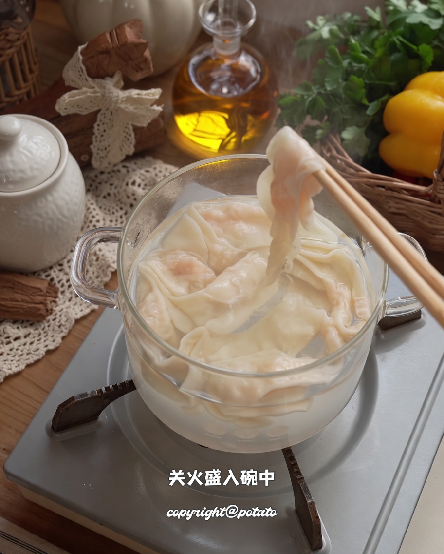 Cooked shrimp paste noodles being lifted from a pot into a serving bowl with chopsticks.